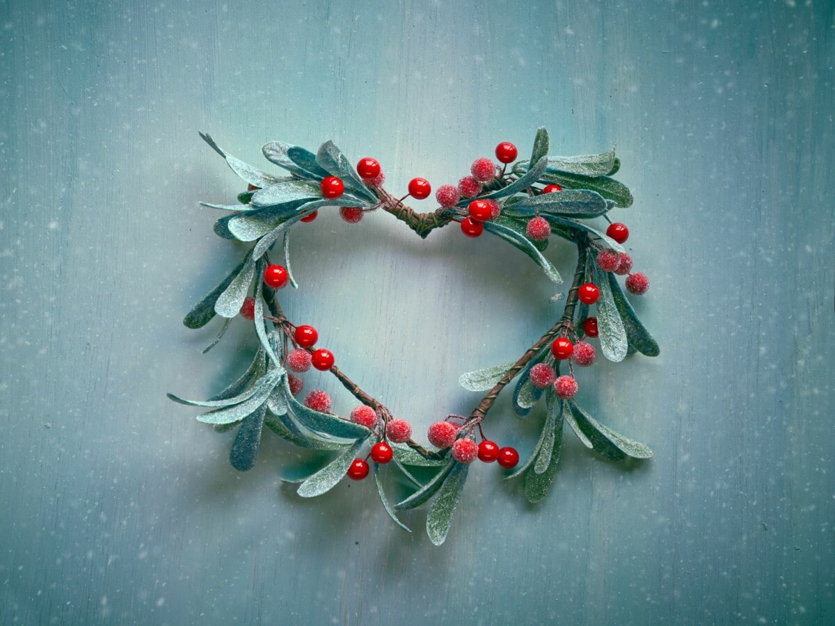 Dekoratives Weihnachtsherz in einer Art Kranz zusammengebunden mit gefroreren Mistelzweigen und roten Beeren.