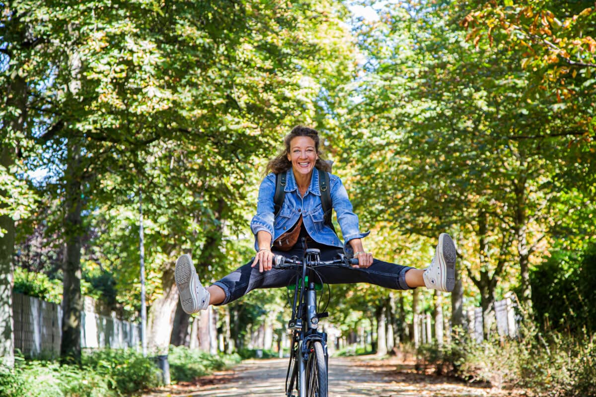 Frau sitzt auf Fahrrad und schwingt vor Freude lachende die Beine hoch nach vorne.